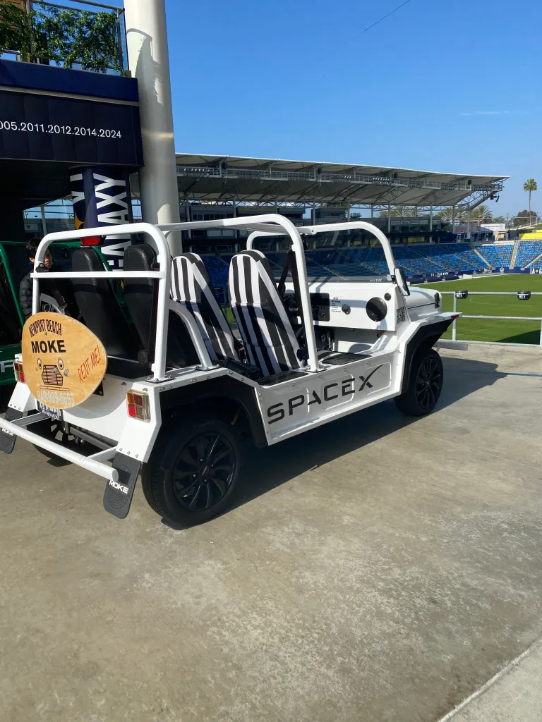 A white Moke electric vehicle with black and white striped seats, branded with 