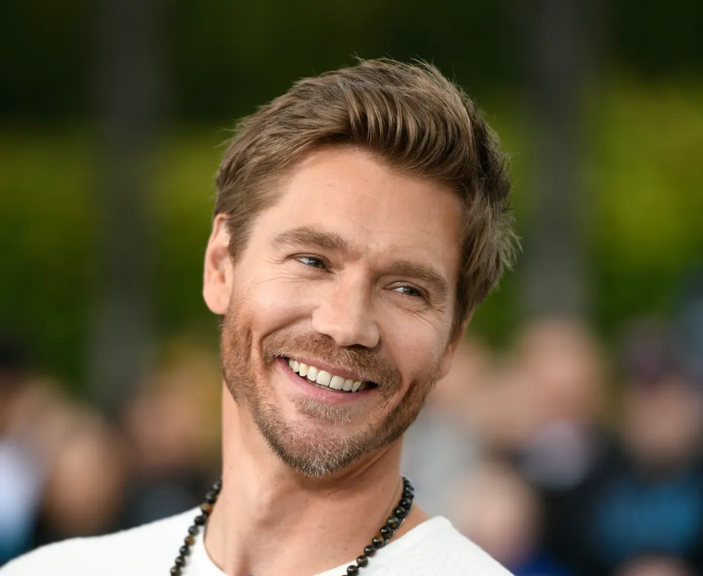 Chad Michael Murray smiling while wearing a white shirt and a beaded necklace.