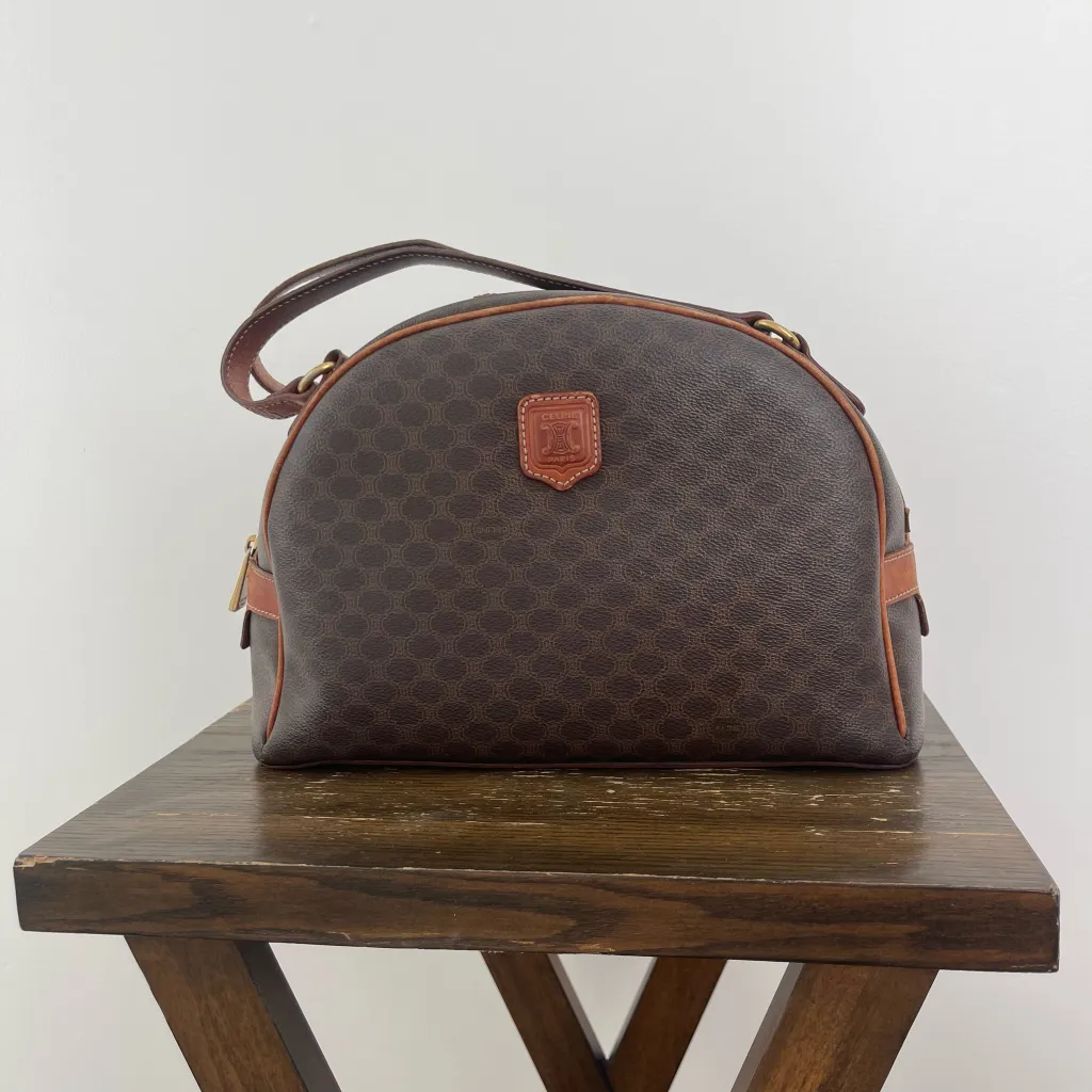 A vintage Celine handbag with a dark brown monogrammed pattern, brown leather trim, and a small brown leather emblem featuring the Celine logo.