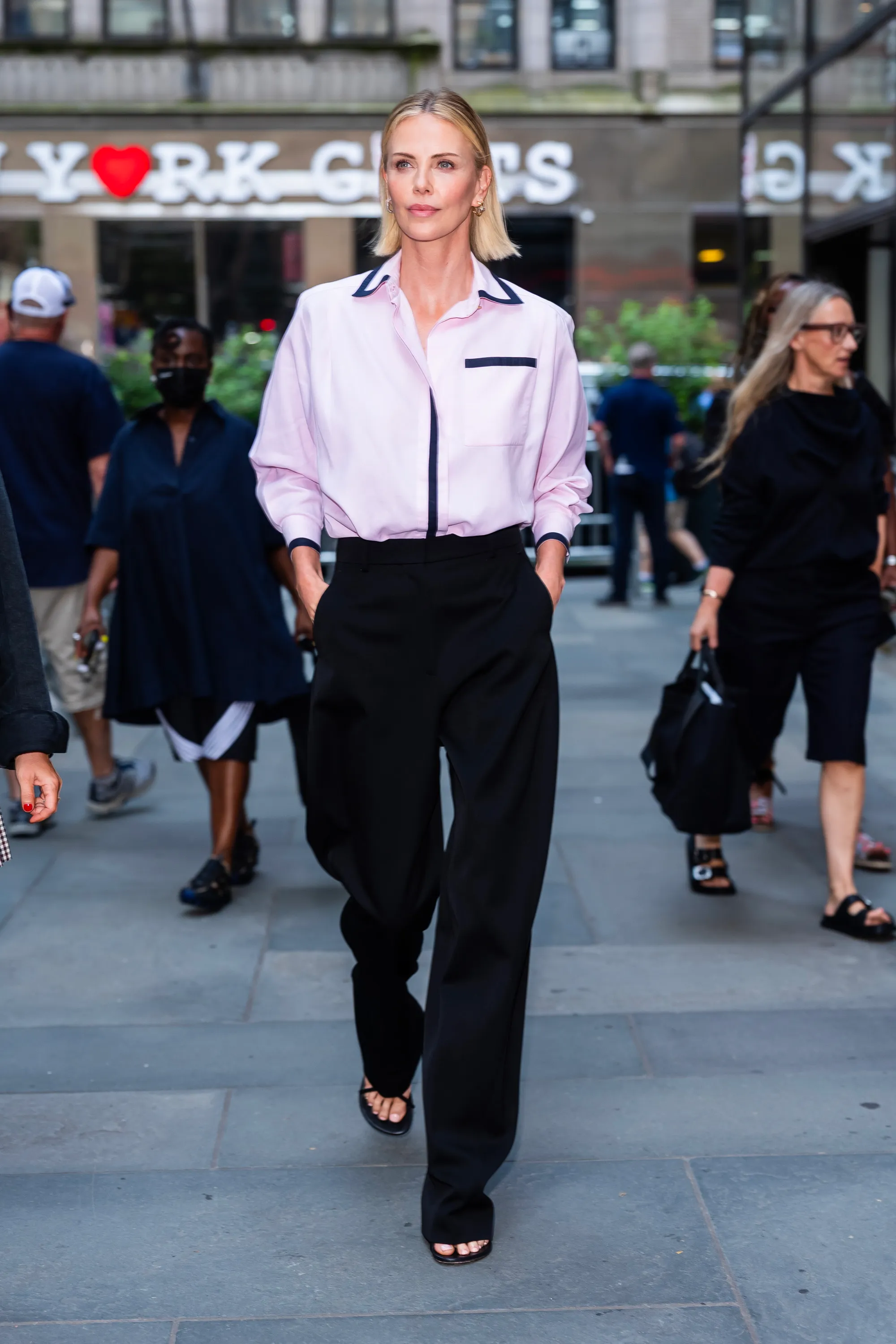 Charlize Theron walking in Midtown, New York, wearing a pink collared shirt and black pants.