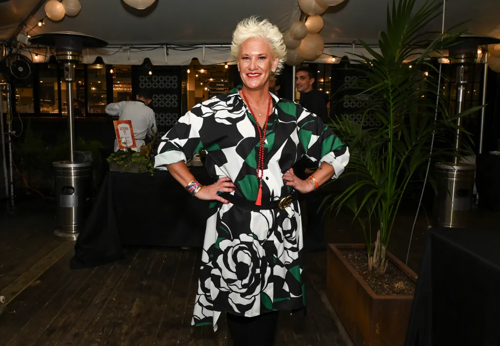 Chef Anne Burrell poses at Aperitivo in a black, white, and green floral-patterned dress, red necklace, and gold belt.