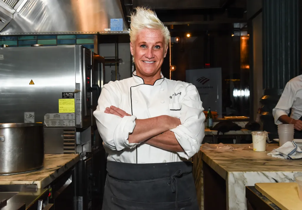 Chef Anne Burrell posing with crossed arms in a kitchen.