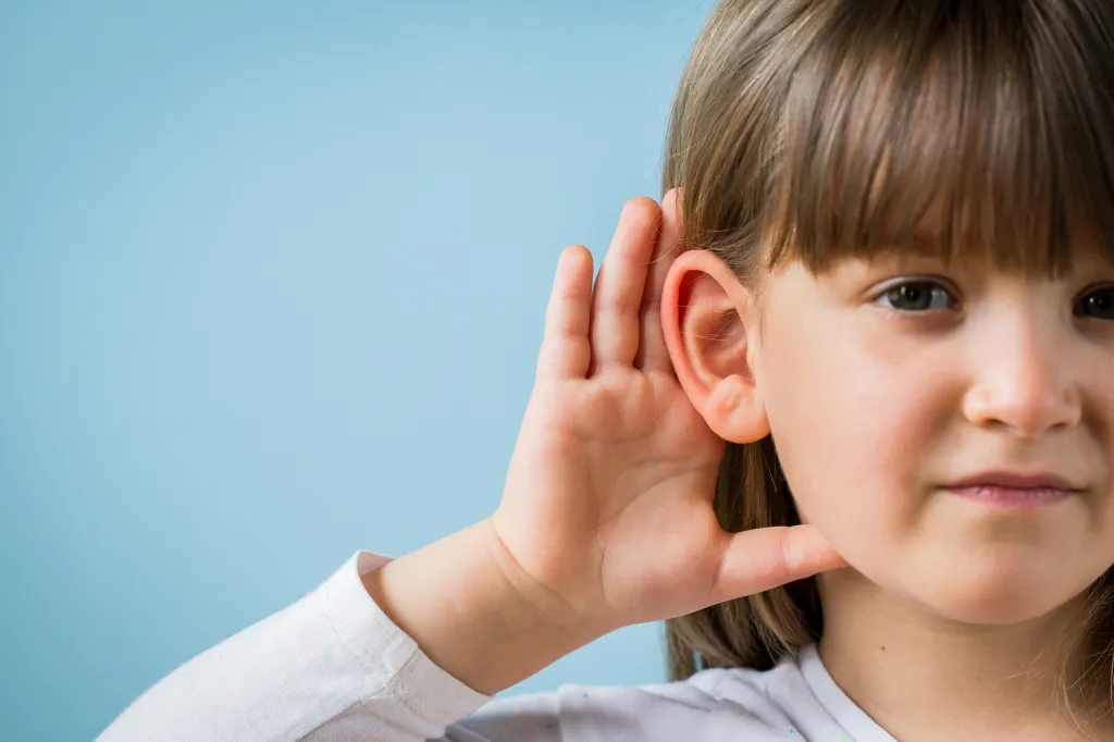 A toddler girl with her hand cupped to her ear, listening.