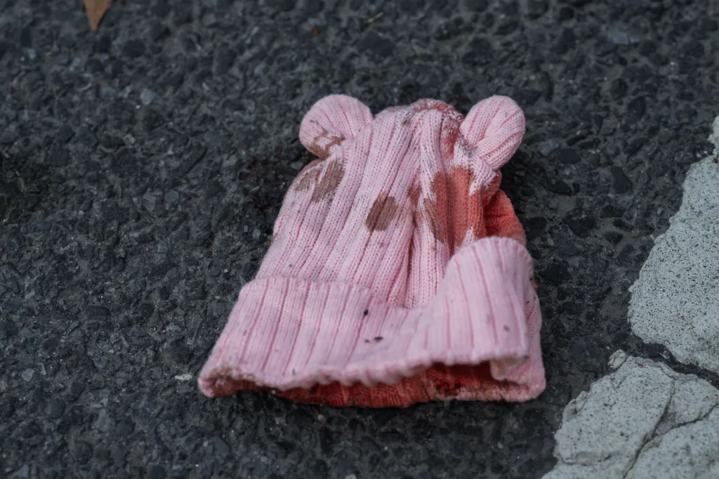 A blood-soaked pink knit hat lies on dark asphalt with a white street line.