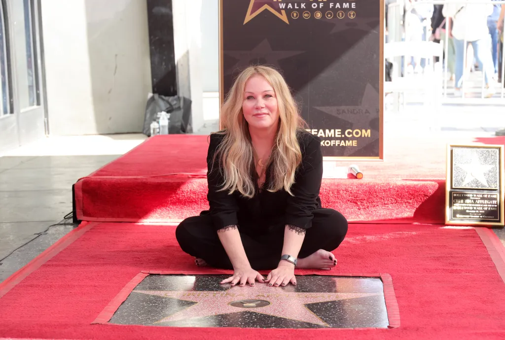 Christina Applegate sits barefoot on a red carpet, touching her Hollywood Walk of Fame star.