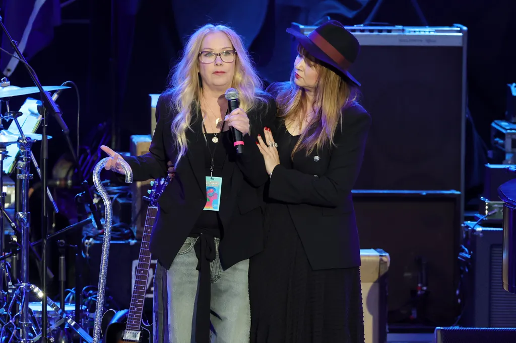 Christina Applegate speaking onstage at the Light Up The Blues 7 Concert, with another woman beside her.