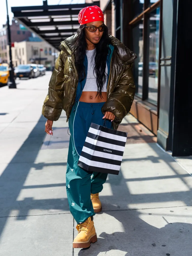 Ciara Miller walking outdoors, holding a Sephora shopping bag.