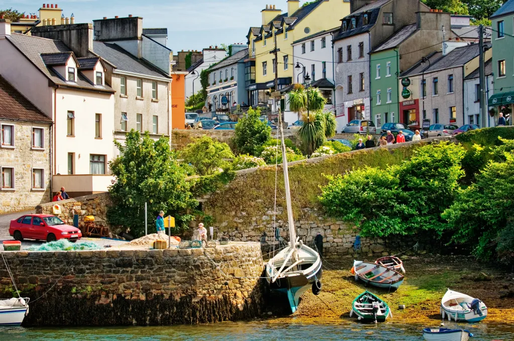 View of the picturesque fishing village of Roundstone, County Galway, Ireland, showing colorful buildings, a stone harbor wall, and boats beached and in the water of Bertraghboy Bay.