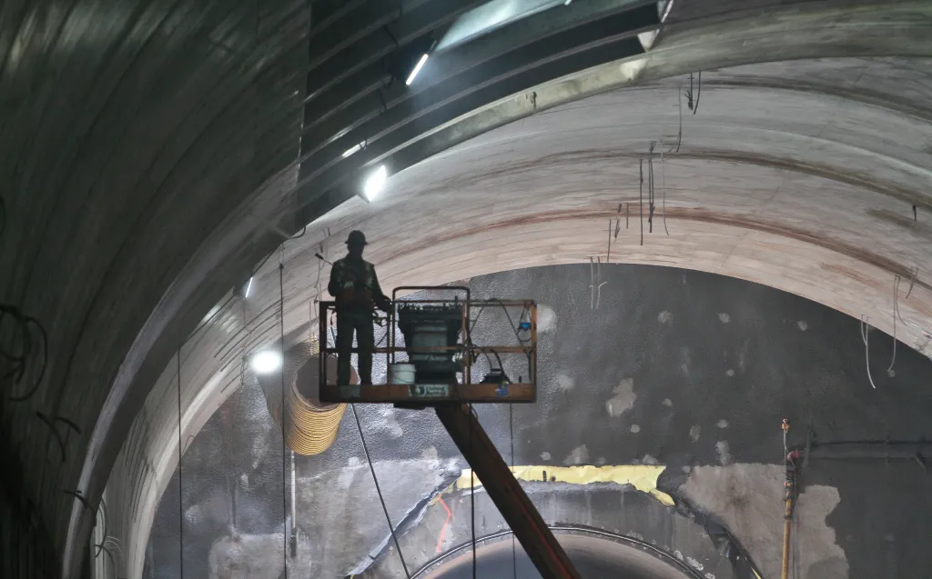 A construction worker in a hard hat and safety vest operates a lift inside a subway tunnel.