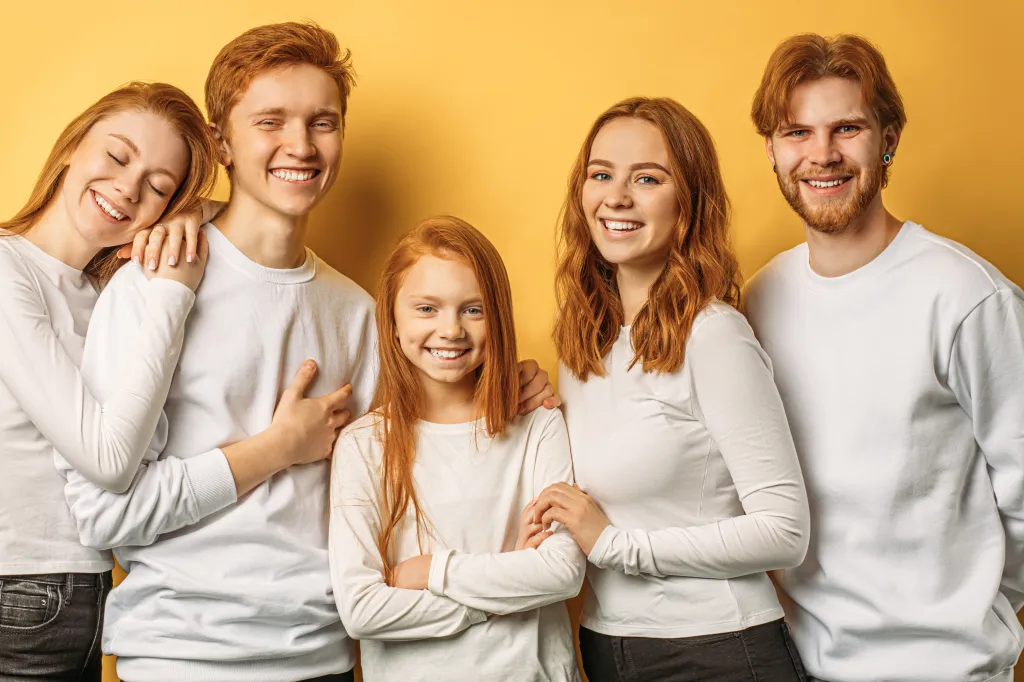 Group of five happy redheaded people, including a young girl, against a yellow background.