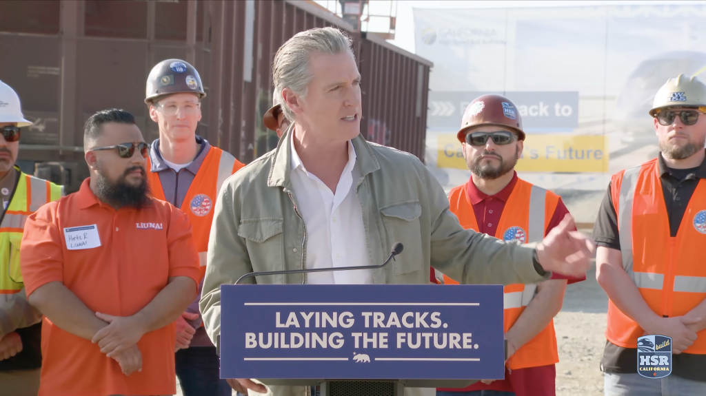 Gavin Newsom speaking at a podium with the text 