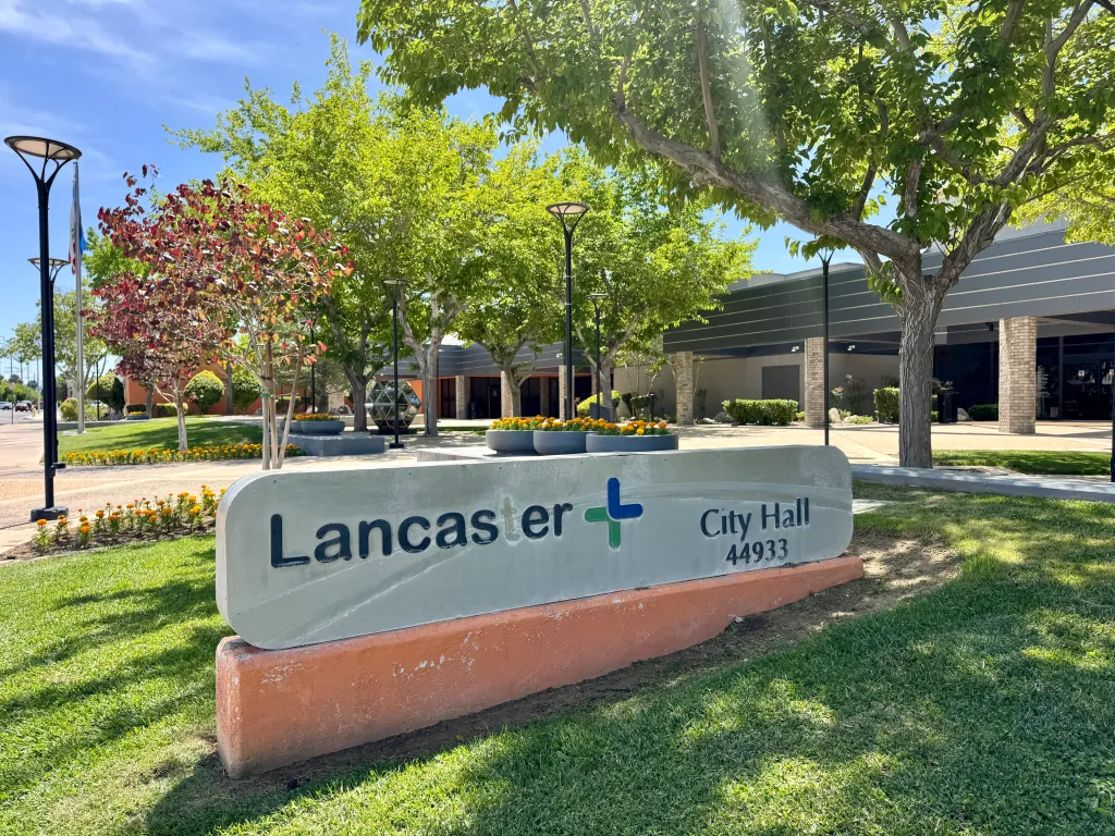 A sign for Lancaster City Hall 44933, with trees and the building in the background.