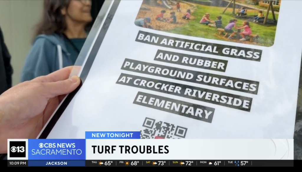 A parent holding a protest sign against artificial turf at Crocker Riverside Elementary School.