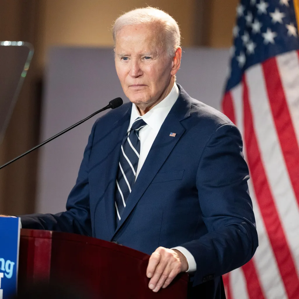 Former President Joe Biden speaking at a podium with an American flag in the background.