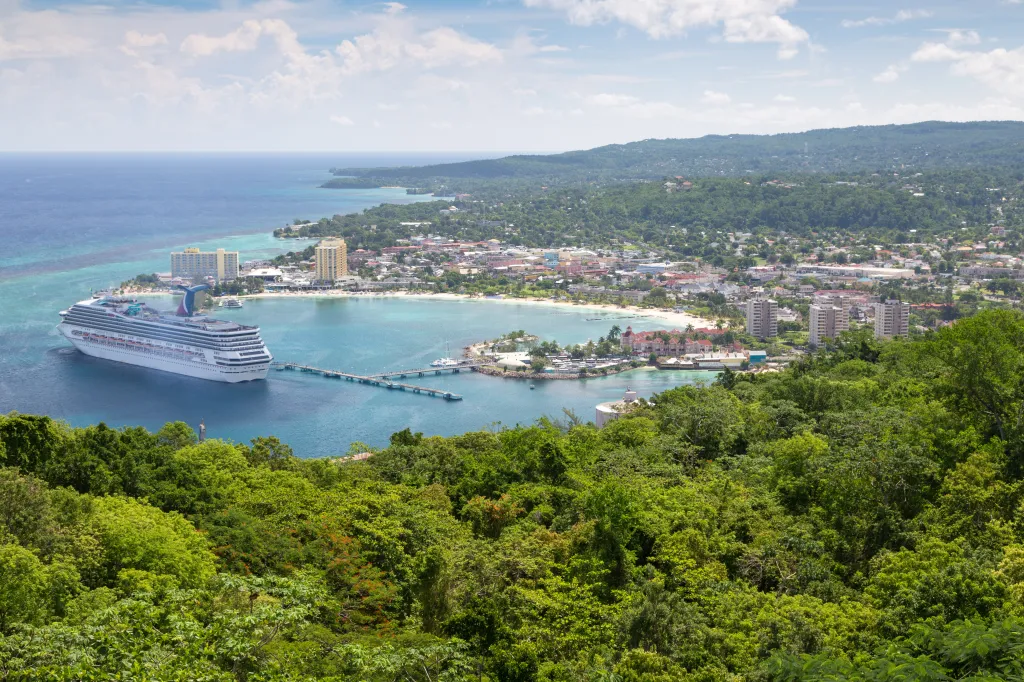 Cruise ship anchored in the harbor of Ocho Rios, Jamaica, with a green tropical hillside in the foreground.