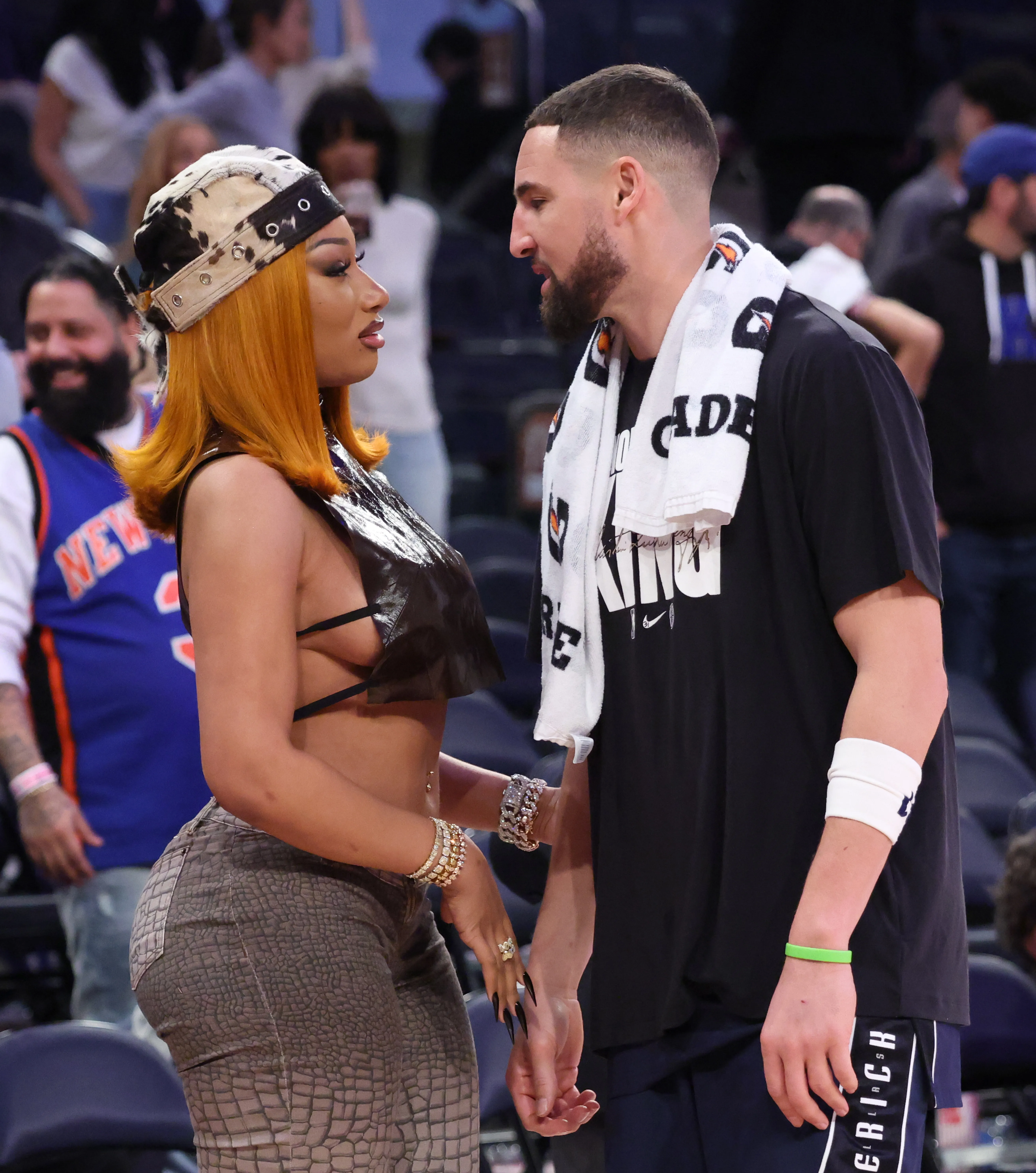 Music artist Megan Thee Stallion and Dallas Mavericks guard Klay Thompson facing each other on a basketball court.