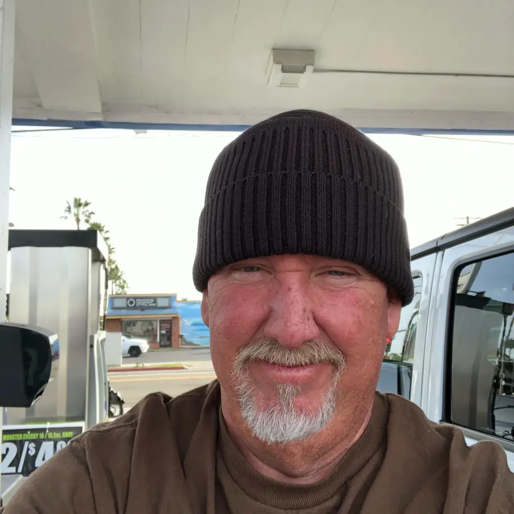 Darrell Sheets wearing a beanie and brown shirt, standing at a gas station.