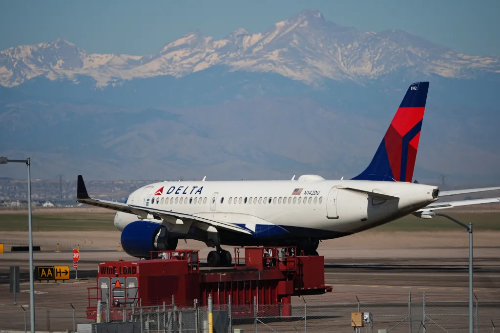 A Delta Airlines jetliner on a runway with snow-capped mountains in the background.