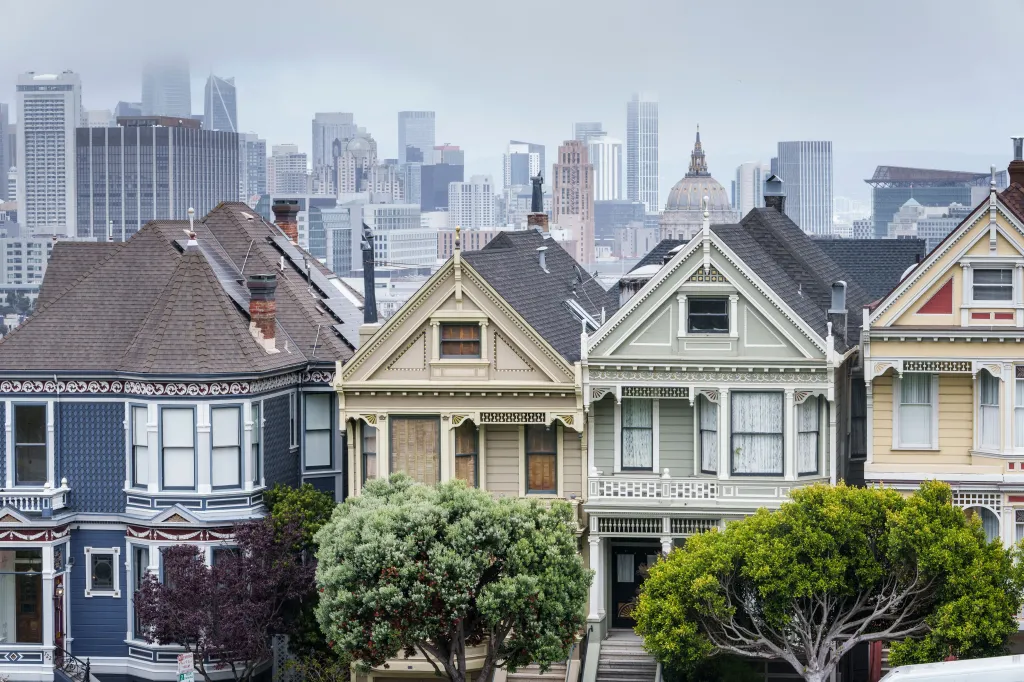 Historic Victorian-style homes in San Francisco with City Hall and the skyline in the background.