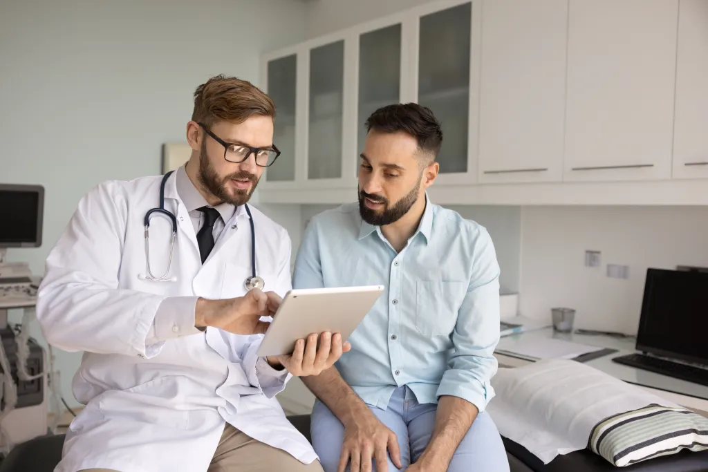 Male doctor discussing therapy plan with a male patient using a tablet.