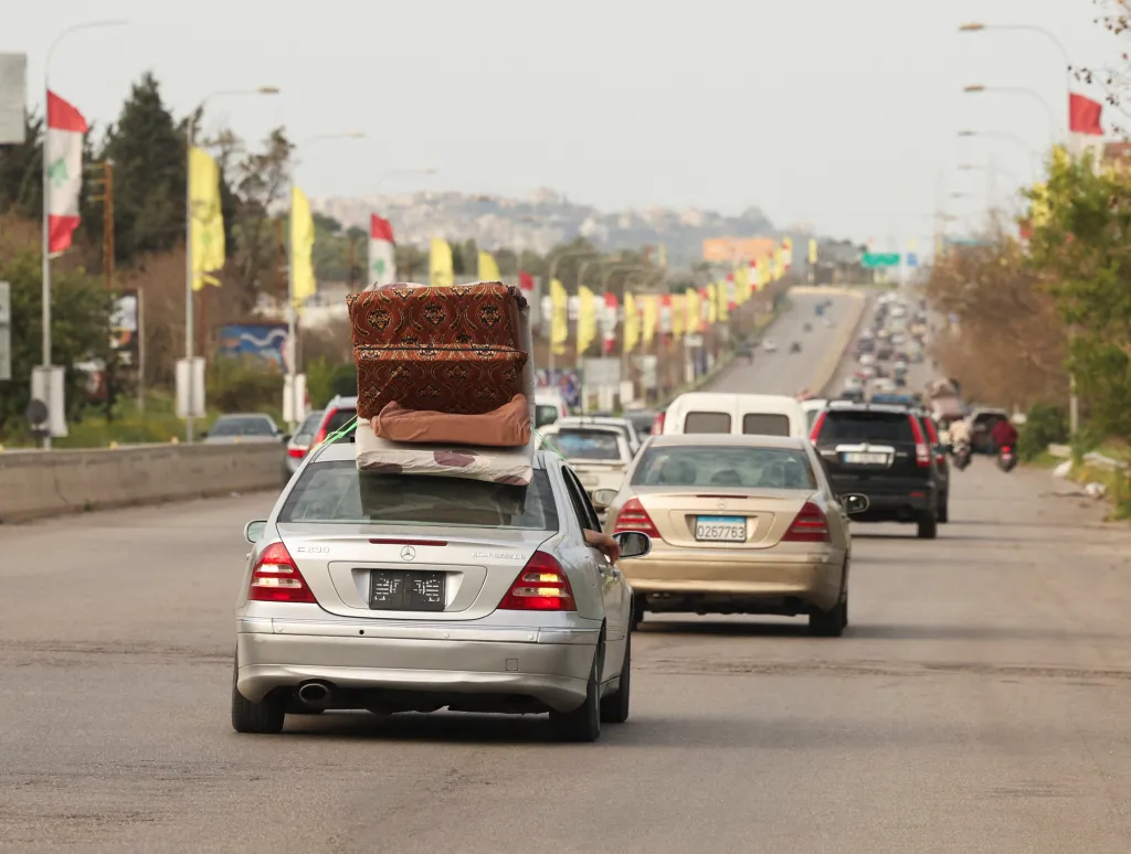 A silver car with luggage strapped to its roof drives on a highway, part of a line of cars of displaced people returning home near Sidon, Lebanon.