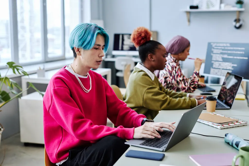 A line of women working at computers in pink, green and plaid shirts