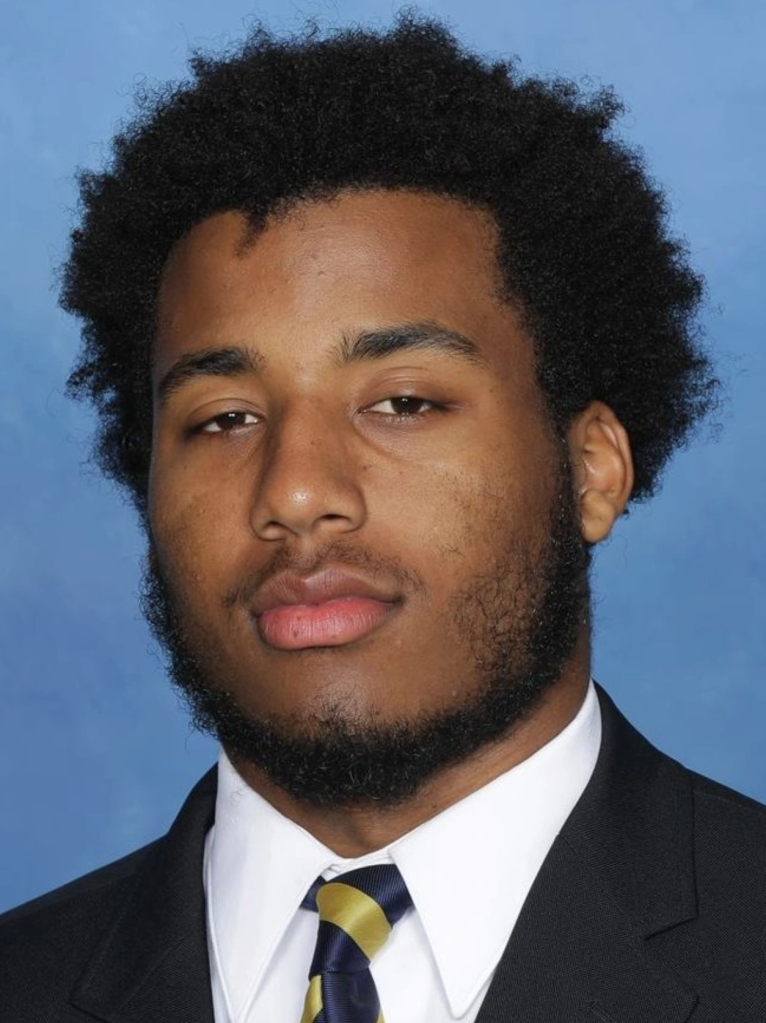 Headshot of Hadari Darden, a young Black man with a beard and dark curly hair, wearing a suit jacket and striped tie against a blue background.