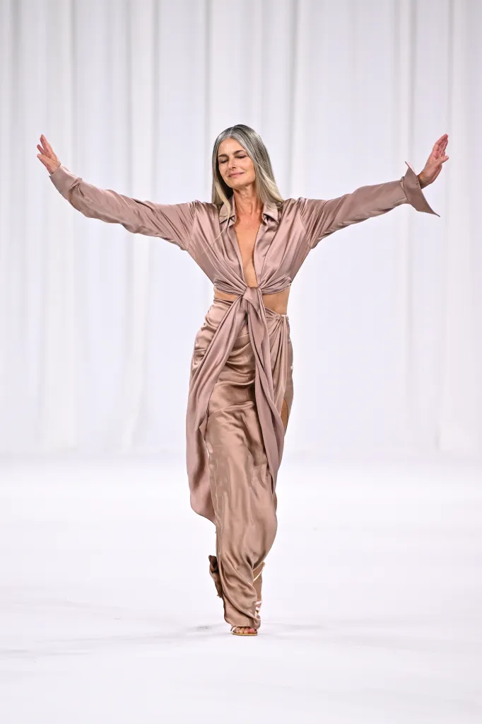 Paulina Porizkova walking the Balmain runway in a champagne satin shirt tied at the waist and a matching draped skirt.