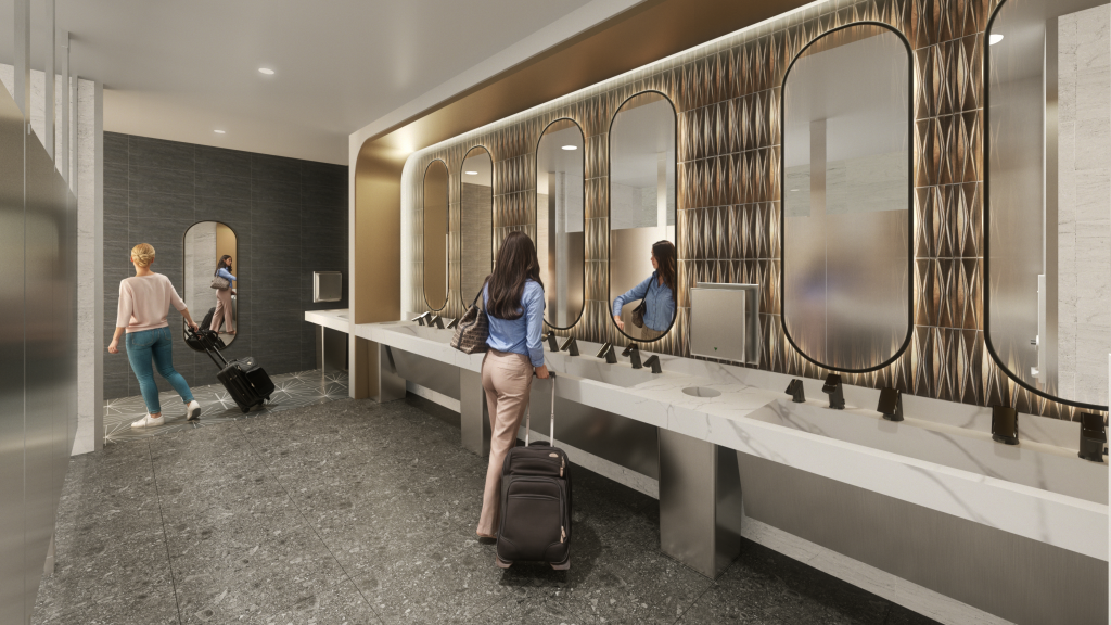 Illustration of a modern women's restroom at Hollywood Burbank Airport with two travelers, a long marble sink with multiple faucets and oval mirrors, and a gray tile floor.