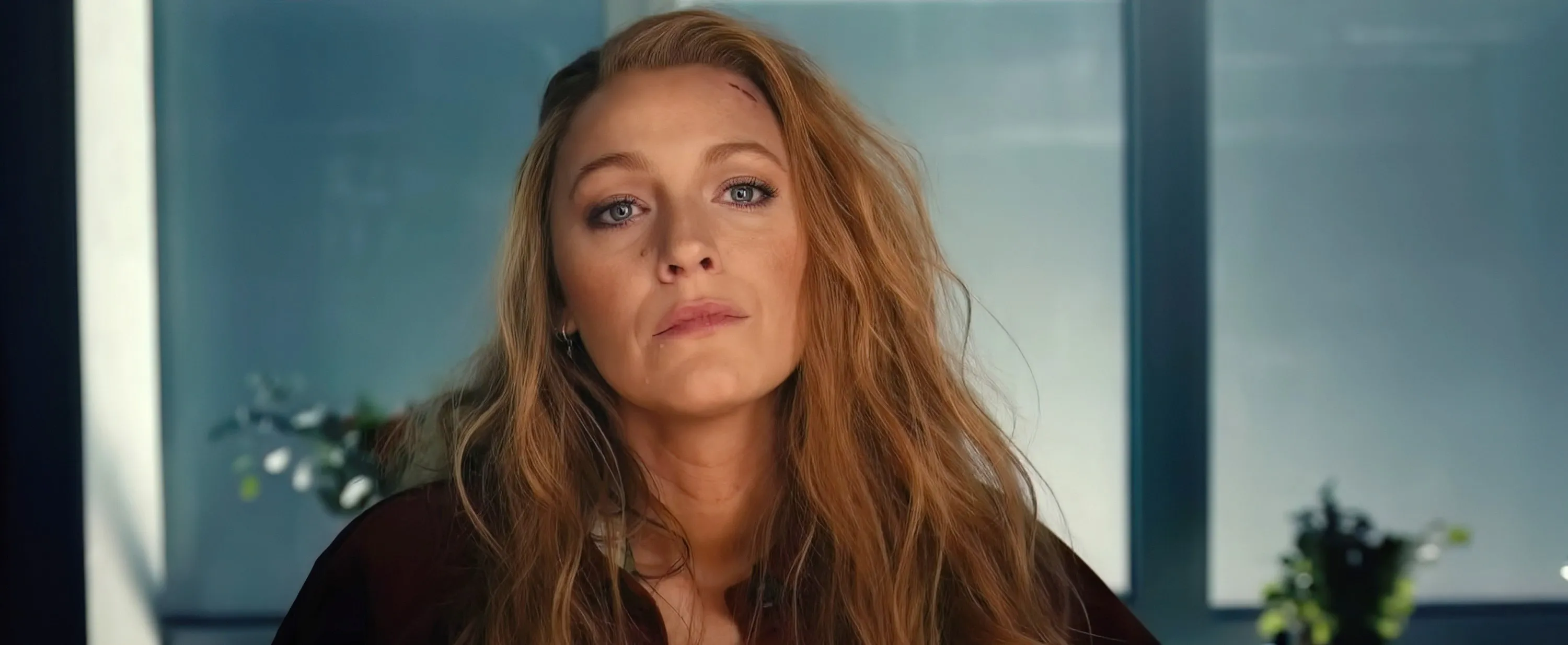 Blake Lively with long wavy hair and an injured face, looking at the viewer.