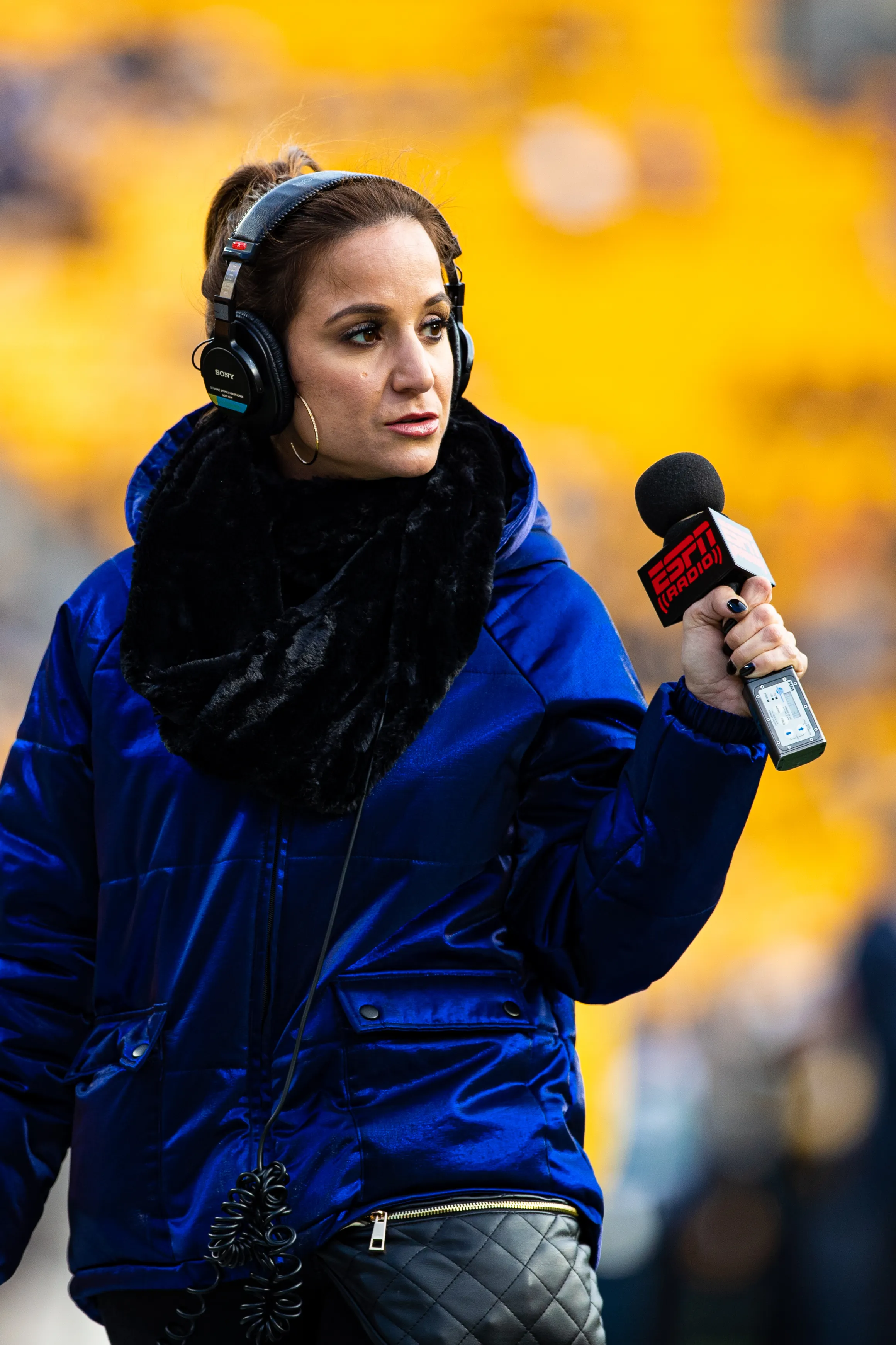 Dianna Russini, an ESPN sideline reporter, in a blue coat and black scarf, wearing headphones and holding an ESPN Radio microphone.
