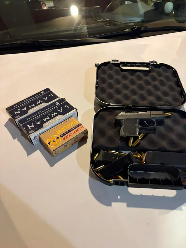 A pistol in a carrying case with ammunition, along with boxes of ammunition, on a white surface.