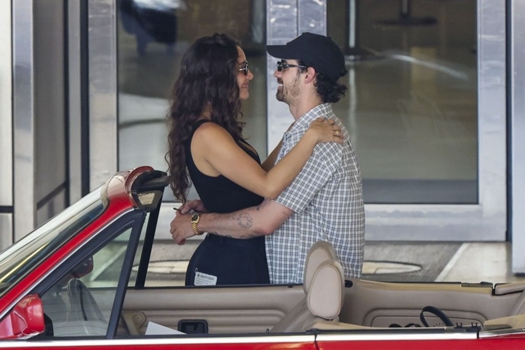 Joe Jonas and Tatiana Gabriela embracing next to a red BMW convertible.