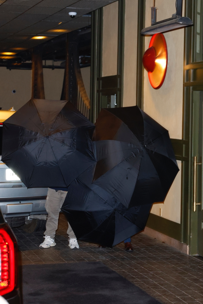 Taylor Swift and Travis Kelce hide behind large black umbrellas while arriving at Casa Cipriani in NYC.