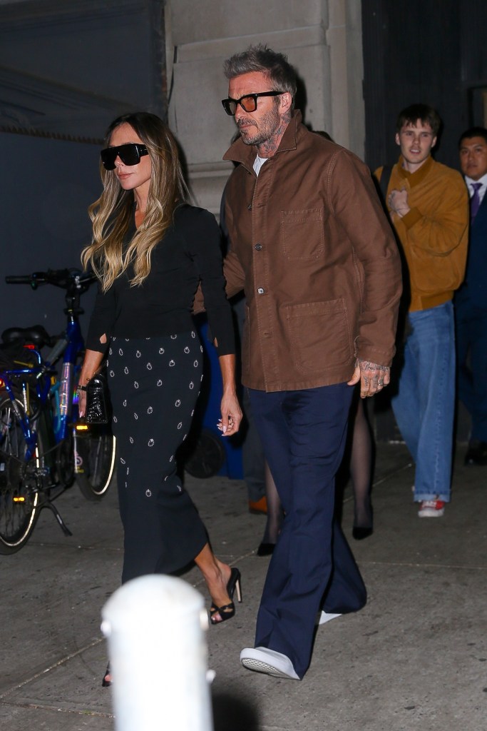 Victoria Beckham, in a black sweater and black patterned skirt, with David Beckham, in a brown jacket and blue jeans. Cruz Beckham wears a brown jacket and blue jeans.