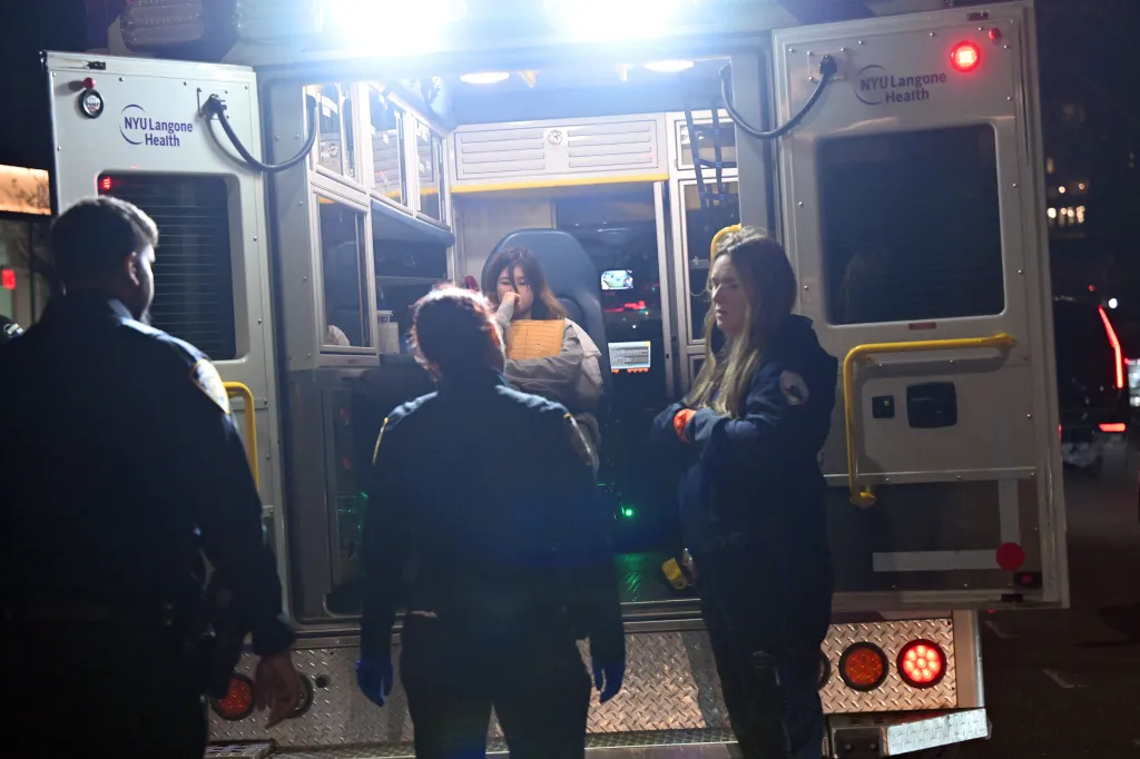 Pei Chung being assisted into an NYU Langone Health ambulance by EMTs and police officers at night.