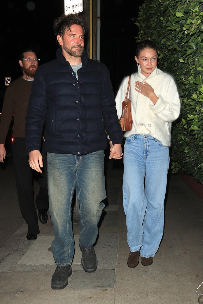 Bradley Cooper and Gigi Hadid holding hands while walking out of a restaurant at night.