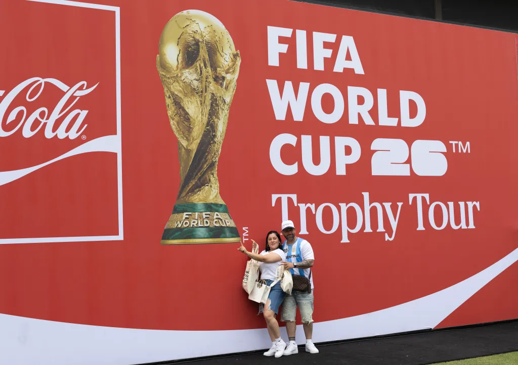 Fans pose in front of a giant FIFA World Cup Trophy Tour 2026 banner.