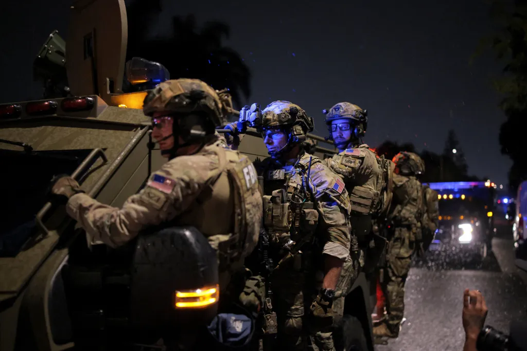 FBI agents in tactical gear stand next to an armored vehicle at night.