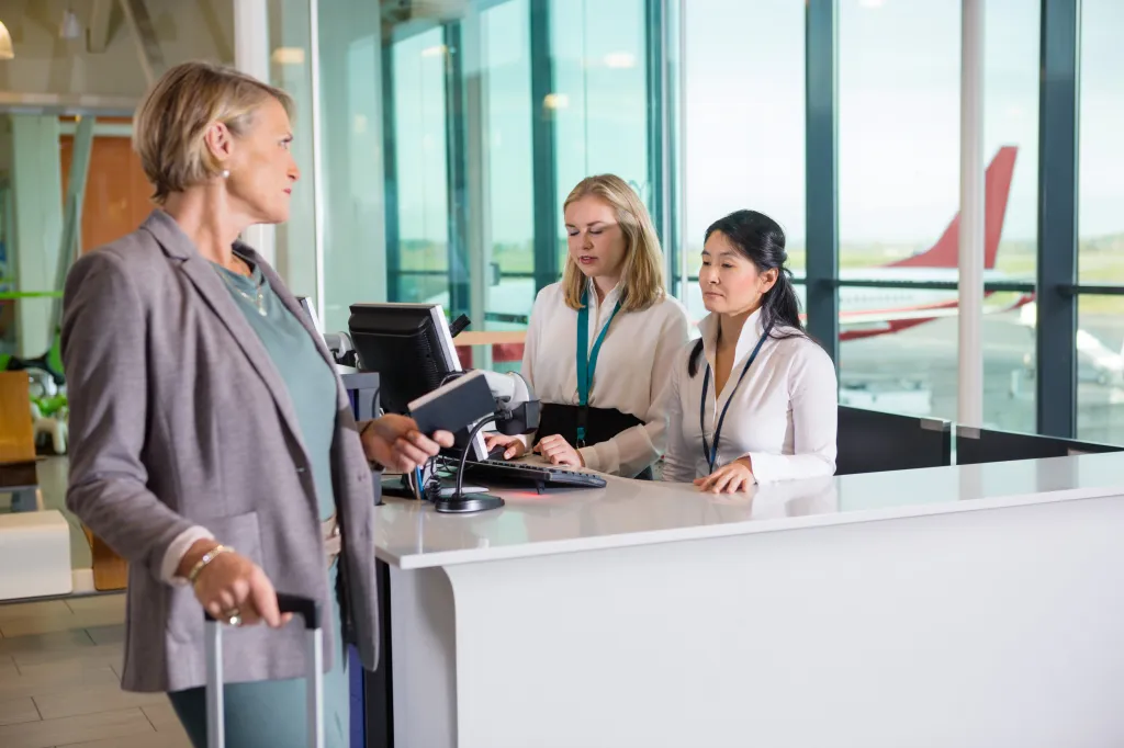 Passenger holding a passport while looking at receptionists working at an airport counter.