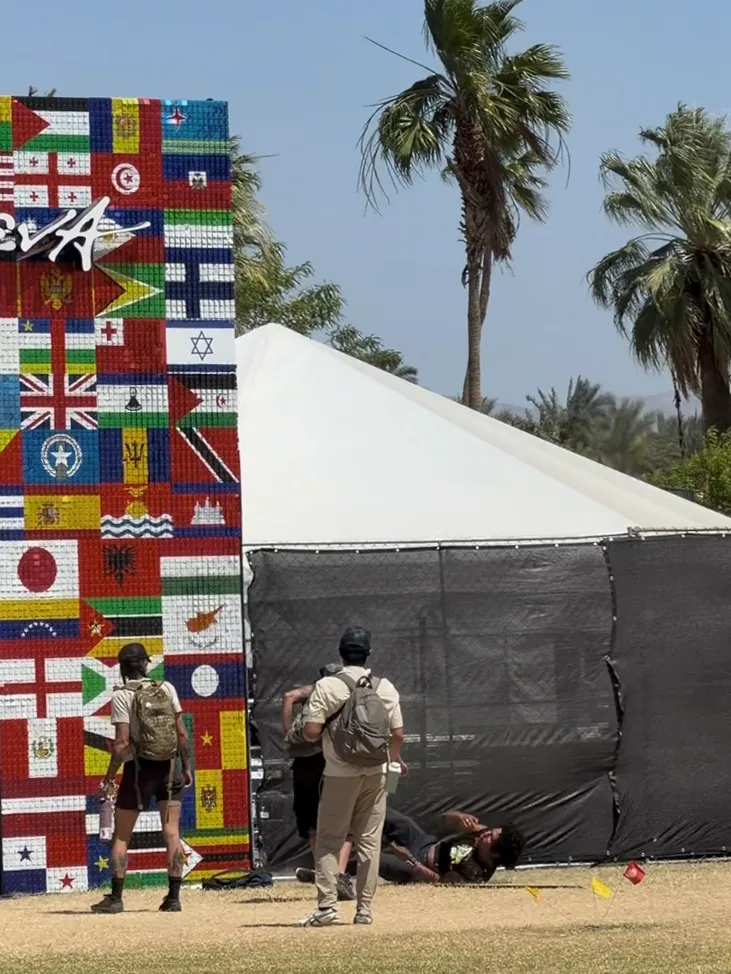 A person lies on the ground next to a wall made of flags after attempting to remove the Israeli flag from a Coachella art installation.