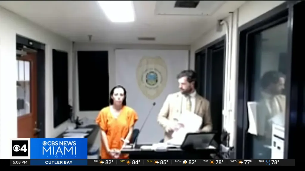 A woman in an orange jumpsuit stands in a courtroom with a man in a suit.