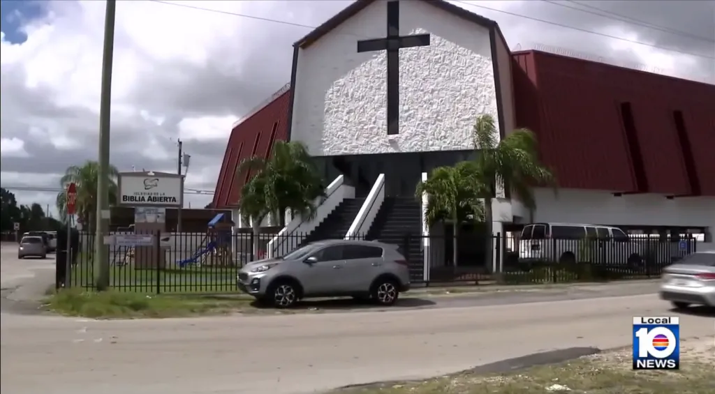 A modern white church with a large black cross and a red roof.