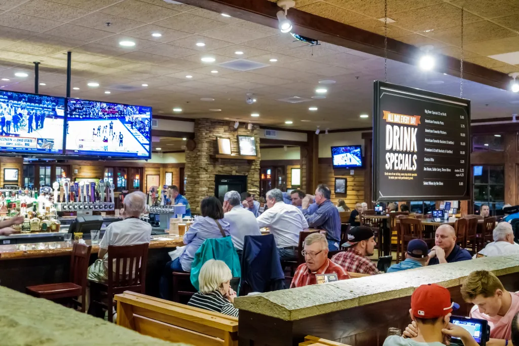 Interior of Smokey Bones Bar & Fire Grill with customers, TVs showing sports, and a sign for drink specials.