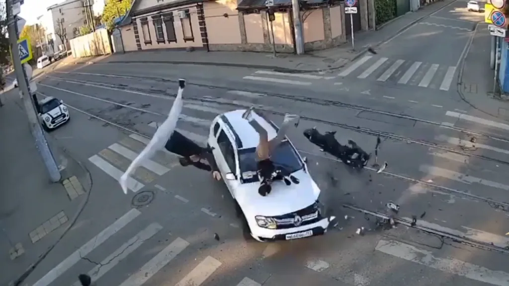 Motorcycle colliding with a car at an intersection, throwing the rider and passenger onto the roadway in Krasnodar, Russia.