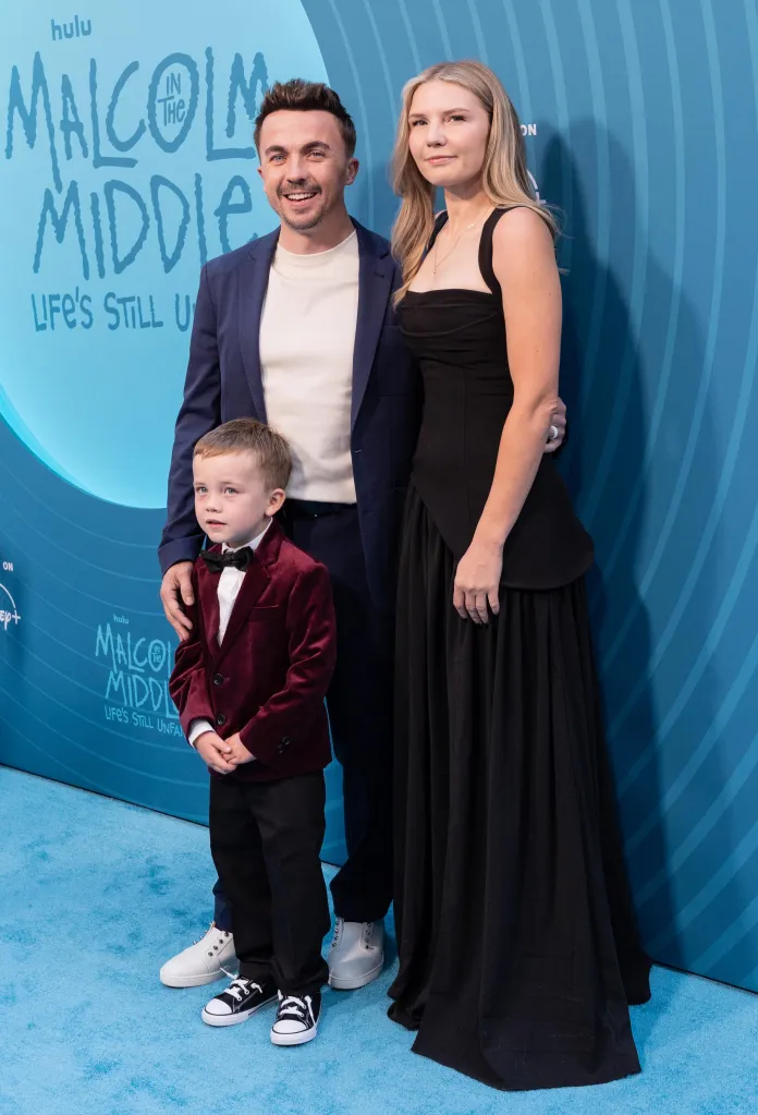 Frankie Muniz, his wife, and son stand on a blue carpet in front of a 