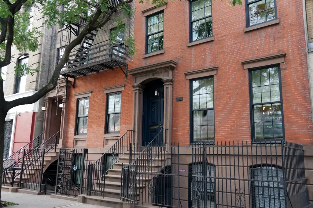 A brick apartment building in New York City with an exterior fire escape and a tree in front.