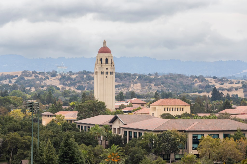 Hoover Tower and Stanford University campus buildings with hills in the background.