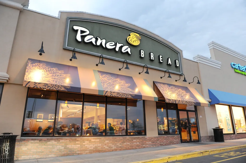 Exterior of a Panera Bread restaurant with its sign and awnings, next to a Carter's store.
