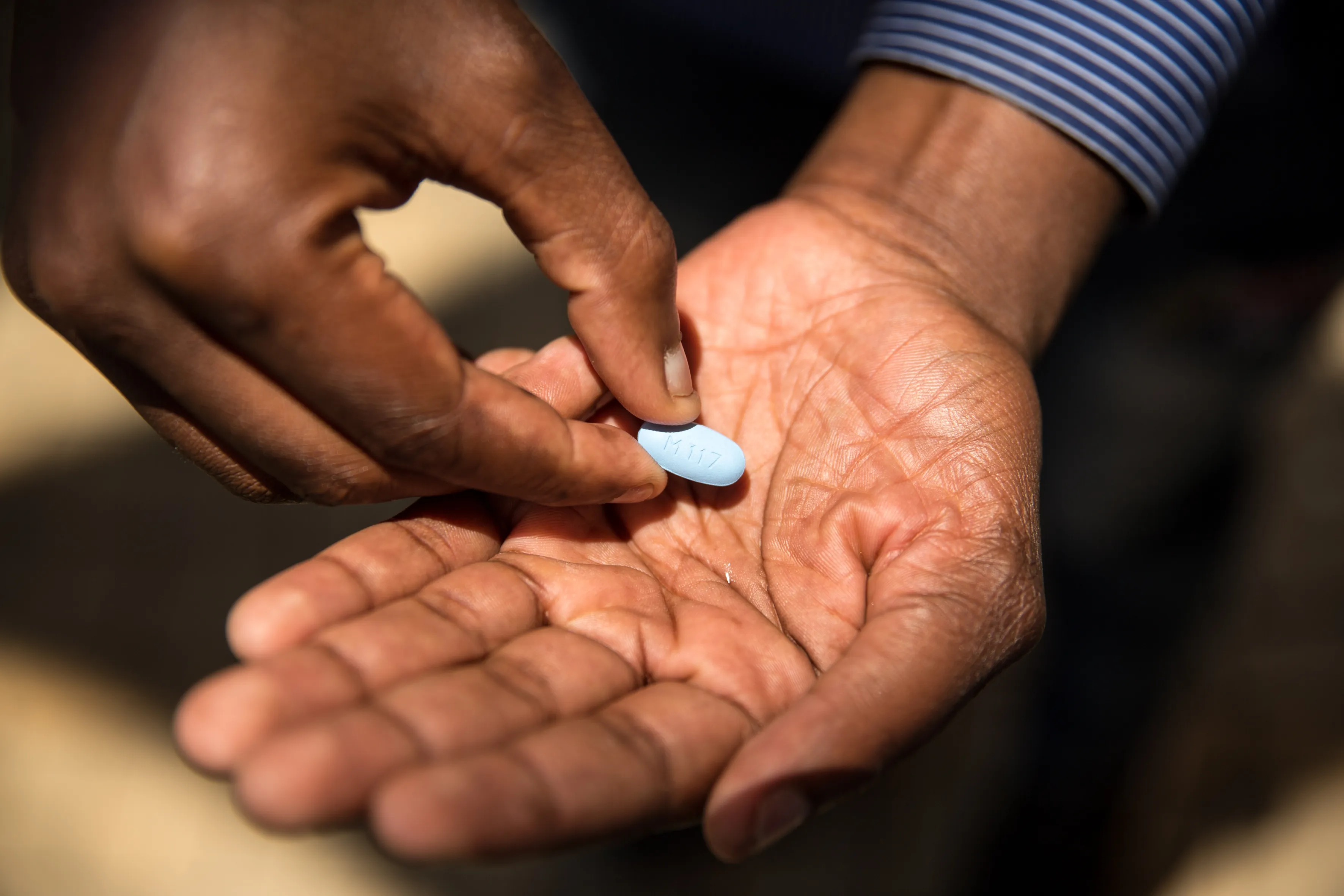 A Black man’s hands hold a blue pill